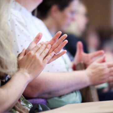 This image shows a close up of people clapping sitting in a lecture theatre.