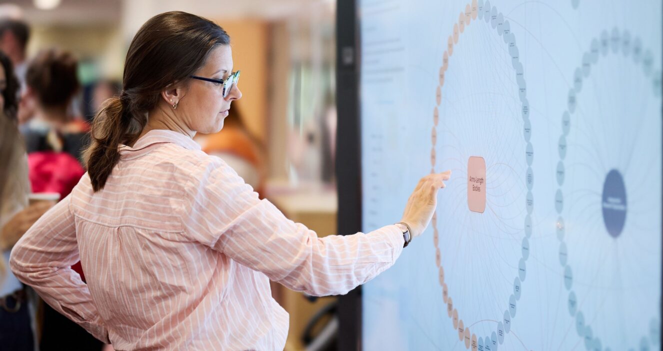 A woman is standing on the left of a screen and pointing to an interactive map.