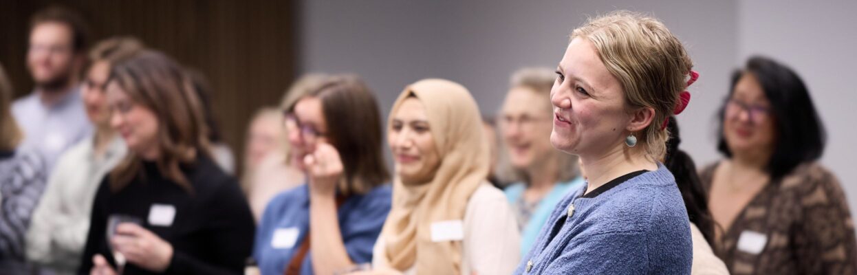 A close up shot of the audience listening to the speeches at the Ministry of Justice's Areas of Research Interest launch. in the foreground is a woman who is smiling and watching wearing a blue cardigan.