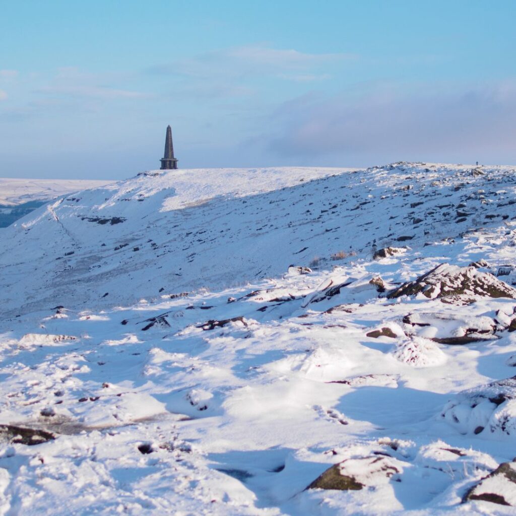 Snowy hills with a light blue sky and scant clouds. In the distance an obselisk stands on the horizon.