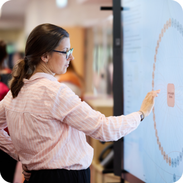 A woman in a pink shirt stood tapping a large interactive screen at the UPEN 2025 Conference.