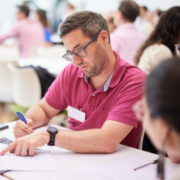 Man in a pink shirt pointing at a worksheet.
