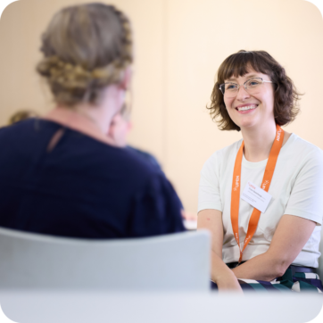 Two people sat talking. One has their back to the camera, the other is smiling.