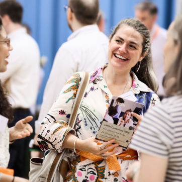 Image shows a group of four people at the UPEN Conference talking. One person in focus is holding up a UPEN Conference programme.