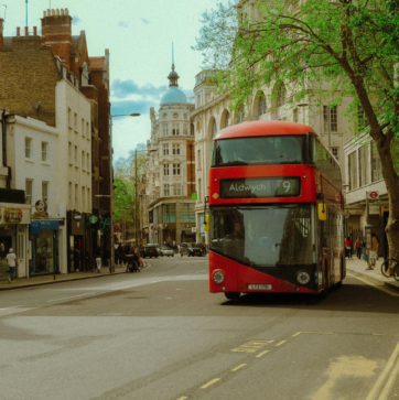 Image is of a London street in Holborn, with multifloored old buildings in the background. A number 9 bus is in the right foreground travelling towards where the photographer is standing. A tree curves over the roof of the bus as it drives past.